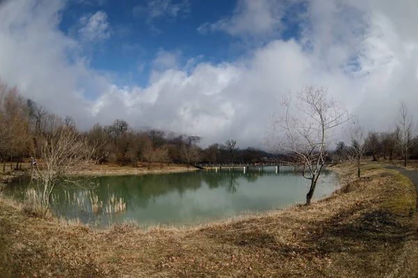 Waldsee mit Brücke während des sonnigen Tages mit Winterbäumen und blauem bewölkten Himmel. schöner natürlicher Bergsee mit Wald im Hintergrund und stürmischen Wolken am Himmel. — Stockfoto