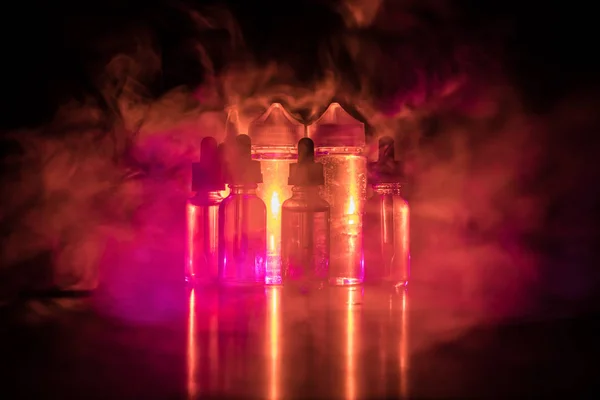 Concepto Vape. Nubes de humo y botellas de vapor líquido sobre fondo oscuro. Efectos luminosos — Foto de Stock