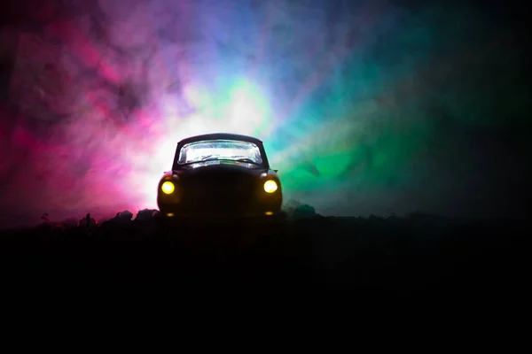 Silhouet van oude oldtimers in mistige donker getinte achtergrond met gloeiende lichten in weinig licht, of silhouet van oude misdaad auto donkere achtergrond. — Stockfoto