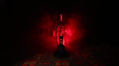 Nargile kömürü nargile kupa Arap iç de buhar bulutları yapma. Şark süsleme halı üzerinde. Şık oryantal shisha içinde karanlık arka ışık ile. Shisha dönme göstermek üzerinde. Kaymak vurdu