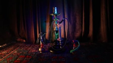 Nargile kömürü nargile kupa Arap iç de buhar bulutları yapma. Şark süsleme halı üzerinde. Şık oryantal shisha içinde karanlık arka ışık ile. Shisha dönme göstermek üzerinde. Kaymak vurdu
