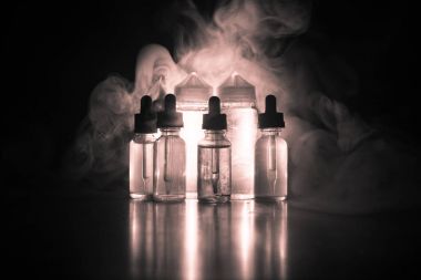 Vape kavramı. Duman bulutları ve vape sıvı şişe koyu arka plan üzerinde. Işık efektleri