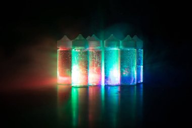 Vape kavramı. Duman bulutları ve vape sıvı şişe koyu arka plan üzerinde. Işık efektleri