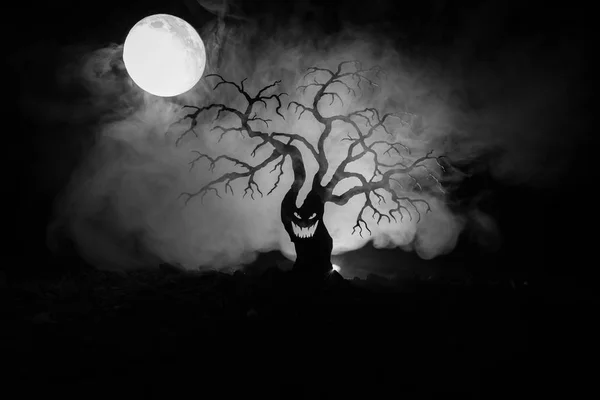 Silhouette of scary Halloween tree with horror face on dark foggy toned background with moon on back side. Scary horror tree with zombie and demon faces. — Stock Photo, Image