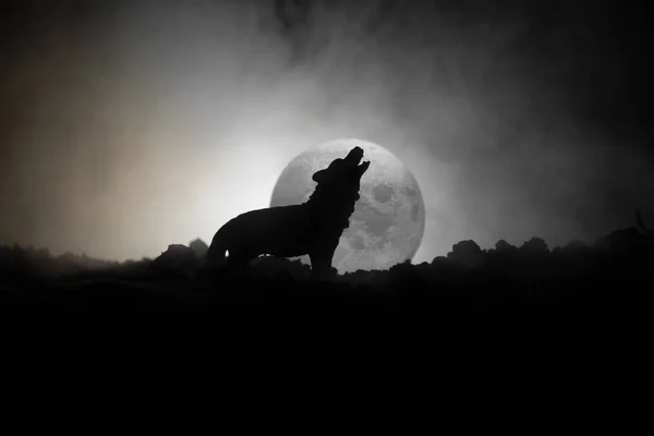 Silhouette di lupo ululante contro sfondo scuro tonica nebbiosa e luna piena o lupo in silhouette ululando alla luna piena. Halloween concetto di orrore . — Foto Stock