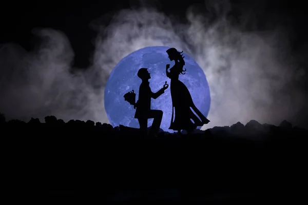 Geweldige scène van de liefde. Silhouetten van man vrouw of silhouetten van paar tegen grote maan bij achtergrond worden voorstel aangebracht — Stockfoto