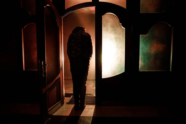 Silhouette of an unknown shadow figure on a door through a closed glass door. The silhouette of a human in front of a window at night. Scary scene halloween concept of blurred silhouette