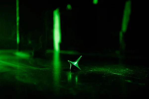 Totem spinning top spinning, wobbling and stopping. Spinning top on mirror surface with toned smoke background light. Whirligig in action in dark room on table. — Stock Photo, Image