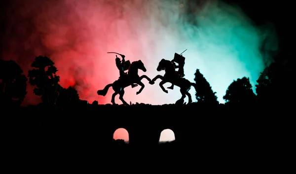 Escena de batalla medieval en puente con caballería e infantería. Siluetas de figuras como objetos separados, lucha entre guerreros sobre fondo de niebla tonificado oscuro. Escena nocturna . — Foto de Stock