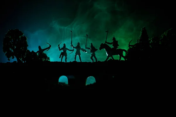 Scena di battaglia medievale su ponte con cavalleria e fanteria. Silhouette di figure come oggetti separati, lotta tra guerrieri su sfondo nebbioso dai toni scuri. Scena notturna . — Foto Stock