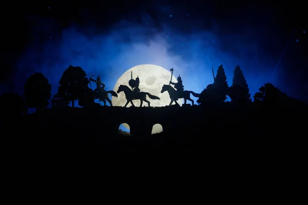 Cena de batalha medieval na ponte com cavalaria e infantaria. Silhuetas de figuras como objetos separados, luta entre guerreiros em fundo enevoado escuro. Cena noturna . — Fotografia de Stock