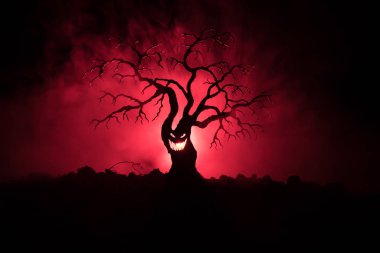 Karanlık sisli yüzündeki korku korkunç Cadılar Bayramı ağacıyla silüeti arka plan arka yüzü aya ile tonda. Zombi ve şeytan yüzü olan korkunç korku ağaç.