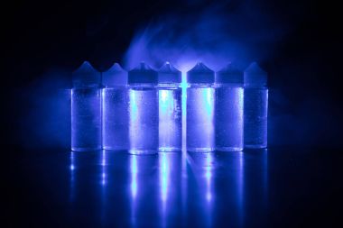 Vape kavramı. Duman bulutları ve vape sıvı şişe koyu arka plan üzerinde. Işık efektleri