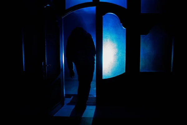 Silhouet van een figuur van de onbekende schaduw op een deur door middel van een gesloten glazen deur. Het silhouet van een mens tegenover een raam bij nacht. Enge scène halloween concept van wazig silhouet — Stockfoto