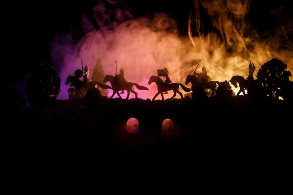 Scène de bataille médiévale sur pont avec cavalerie et infanterie. Silhouettes de figures comme objets séparés, lutte entre guerriers sur fond brumeux foncé. Scène nocturne . — Photo