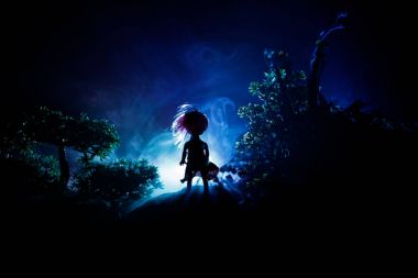Korku Halloween kavramsal görüntü dekore edilmiştir. Işık gece ormanda yalnız kız. Kız gerçeküstü Işıklı ağaçlar arasında ayakta silüeti. Seçici odak.