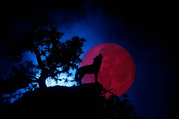 Silhouet van huilende wolf tegen donker getinte mistige achtergrond en volle maan of Wolf in silhouet huilend naar de volle maan. Halloween horror concept. — Stockfoto
