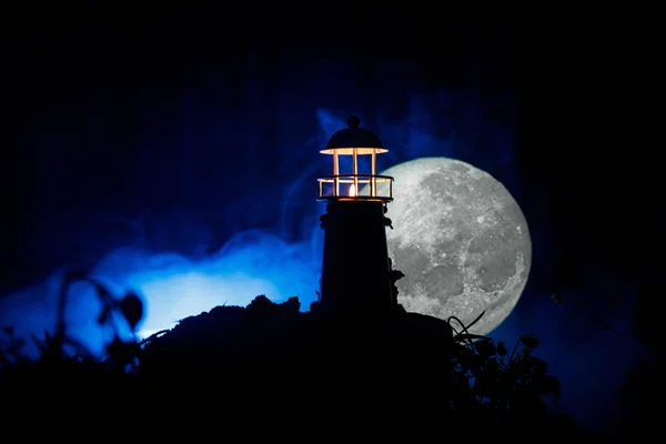 Leuchtturm mit Lichtkegel bei Nacht mit Nebel. alter Leuchtturm auf dem Berg. Tischdekoration. Selektiver Fokus — Stockfoto