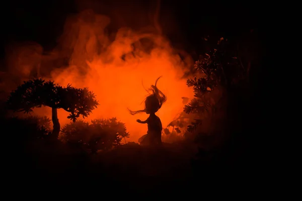 Horror Halloween decorato immagine concettuale. Una ragazza sola con la luce nella foresta di notte. Silhouette di ragazza in piedi tra gli alberi con luce surreale. Focus selettivo . — Foto Stock