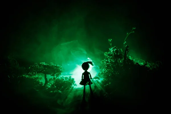 Horror Halloween decorado imagem conceitual. Sozinha com a luz na floresta à noite. Silhueta de menina de pé entre árvores com luz surreal. Foco seletivo . — Fotografia de Stock