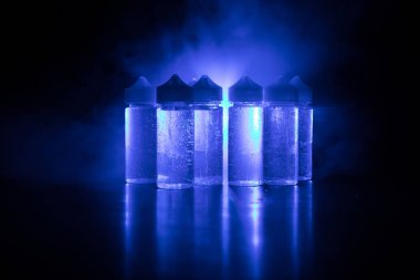 Vape kavramı. Duman bulutları ve vape sıvı şişe koyu arka plan üzerinde. Işık efektleri