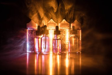 Vape kavramı. Duman bulutları ve vape sıvı şişe koyu arka plan üzerinde. Işık efektleri