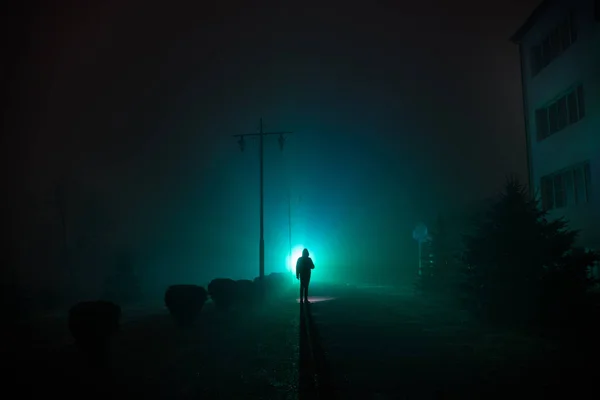 Città di notte nella fitta nebbia. Paesaggio mistico luci surreali con uomo inquietante. La sagoma dell'uomo che cammina in nebbia di notte a luce artificiale. Bella illuminazione mista dal retro . — Foto Stock