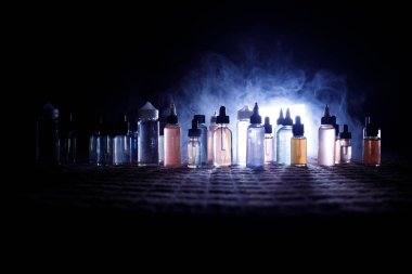 Vape kavramı. Duman bulutları ve vape sıvı şişe koyu arka plan üzerinde. Işık efektleri. Arka plan veya vape reklam veya vape arka plan olarak yararlı.