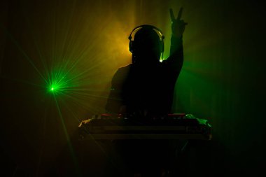 DJ Spinning, Mixing, and Scratching in a Night Club, Hands of dj tweak various track controls on dj's deck, strobe lights and fog, or Dj mixes the track in the nightclub at party clipart