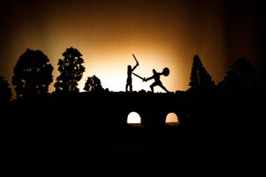 Ortaçağ savaş sahnesi süvari ve piyade ile köprüde. Siluetleri şekiller ayrı nesneler olarak mücadele koyu tonda sisli arka plan savaşçılar arasında. Gece çekimi.