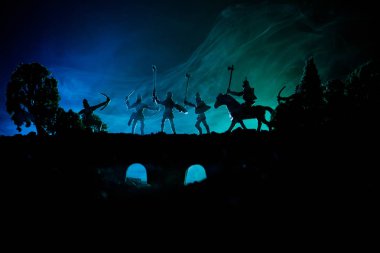 Ortaçağ savaş sahnesi süvari ve piyade ile köprüde. Siluetleri şekiller ayrı nesneler olarak mücadele koyu tonda sisli arka plan savaşçılar arasında. Gece çekimi.