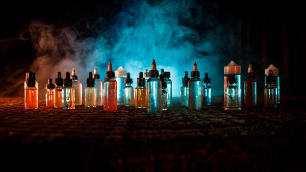 Vape concept. Roken wolken en vape vloeibare flessen op donkere achtergrond. Lichteffecten. Nuttig als achtergrond of vape advertentie of vape achtergrond. — Stockfoto