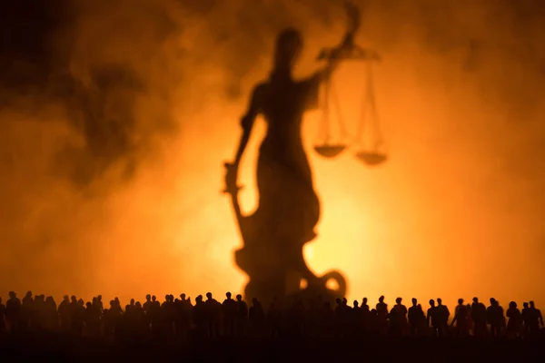 Silueta de estatua de justicia gigante borrosa con espada y escala de pie detrás de la multitud en la noche con fondo de fuego nebuloso. por la noche — Foto de Stock