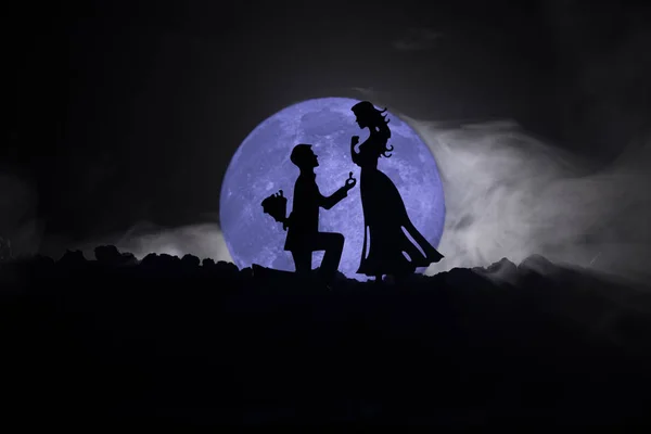 Geweldige scène van de liefde. Silhouetten van man vrouw of silhouetten van paar tegen grote maan bij achtergrond worden voorstel aangebracht — Stockfoto