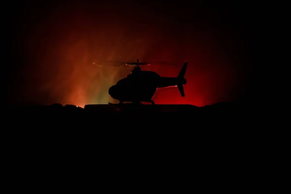 Silhouette of military helicopter ready to fly from conflict zone. Decorated night footage with helicopter starting in desert with foggy toned backlit. Selective focus. — Stock Photo, Image