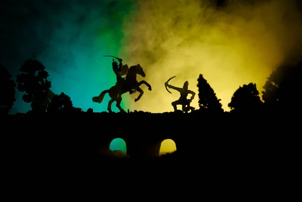 Middeleeuwse slag scène op de brug met de cavalerie en infanterie. Silhouetten van figuren als afzonderlijke objecten, strijd tussen krijgers op donker getinte mistige achtergrond. Nachtbeeld. — Stockfoto