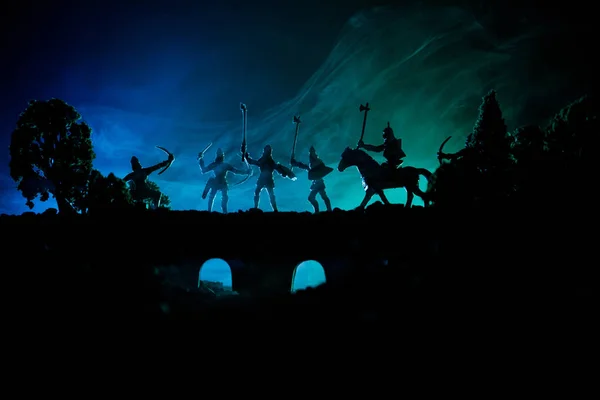 騎兵と歩兵と橋に中世の戦闘シーン。個別のオブジェクトとして人物のシルエットは、暗いトーンの霧の背景に戦士の間戦います。夜のシーン. — ストック写真