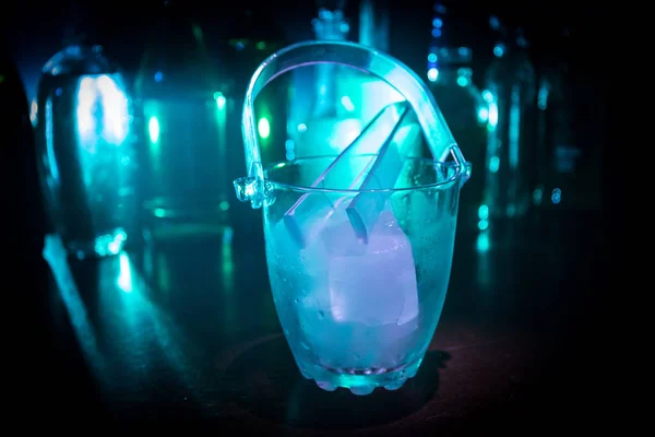 Скляне льодове відро на розмитому фоні з пляшками алкоголю з вогнями та димом. Клуб п'є концепцію. Клубний барний стіл. Готовий служити . — стокове фото