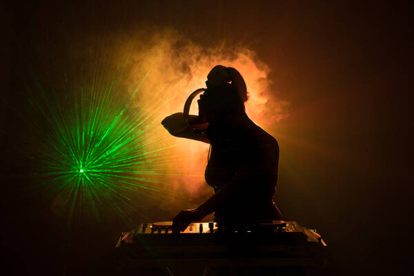 DJ Spinning, Mixing, and Scratching in a Night Club, Hands of dj tweak various track controls on dj's deck, strobe lights and fog, or Dj mixes the track in the nightclub at party. Selective focus