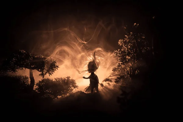 Horror Halloween inredda begreppsmässiga image. Ensam tjej med ljuset i skogen på natten. Silhuetten av flicka stående mellan träden med surrealistiska ljus. Selektivt fokus. — Stockfoto