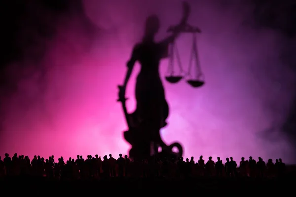 Silhouette of blurred giant lady justice statue with sword and scale standing behind crowd at night with foggy fire background. at night — Stock Photo, Image