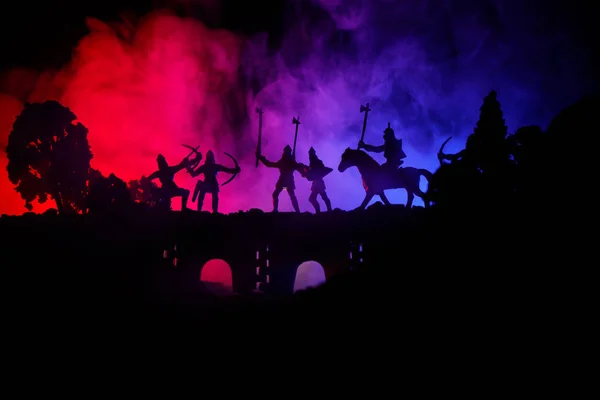 Escena de batalla medieval en puente con caballería e infantería. Siluetas de figuras como objetos separados, lucha entre guerreros sobre fondo de niebla tonificado oscuro. Escena nocturna . — Foto de Stock