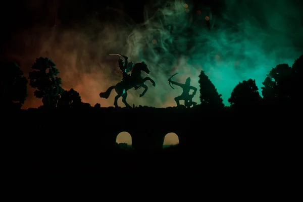 Средневековая боевая сцена на мосту с кавалерией и пехотой. Силуэты фигур как отдельные объекты, борьба между воинами на темном, тонированном туманном фоне. Ночная сцена . — стоковое фото