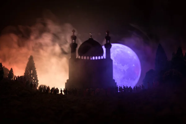 Silhouette einer großen Menschenmenge, die in der Nacht im Wald vor einem verschwommenen Moscheegebäude mit getönten Lichtstrahlen auf nebligem Hintergrund steht. ramadan kareem hintergrund. — Stockfoto