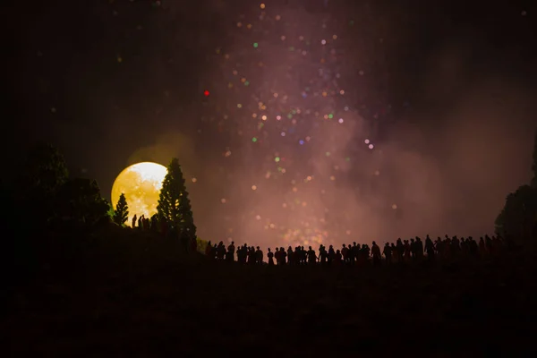 Silhuetten av en stor skara människor i skogen på kvällen titta på stigande stor fullmåne. Inredda bakgrund med natthimlen med stjärnor, måne och utrymme element. Selektivt fokus. — Stockfoto