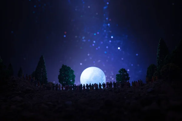 Silhouette di una grande folla di persone nella foresta di notte a guardare al sorgere grande luna piena. Sfondo decorato con cielo notturno con stelle, luna ed elementi spaziali. Focus selettivo . — Foto Stock