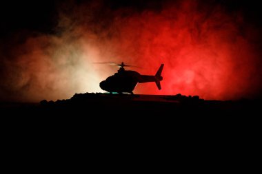Askeri helikopterin silueti çatışma bölgesinden uçmaya hazır. Çölden başlayan sisli arka ışıklandırmalı helikopterle dekore edilmiş gece görüntüleri. Seçici odaklanma. Savaş konsepti