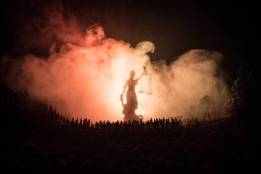 Adalet ve hukuk kavramı. Bulanık dev Bayan adalet heykeli kılıç ve sisli yangın arka plan ile gece kalabalık duran ölçek silüeti. Seçici odak