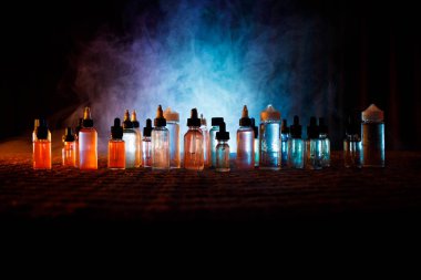 Vape konsepti. Karanlık arka planda duman bulutları ve tüp sıvısı şişeleri. Işık efektleri. Arka plan, vape reklamı ya da vape arkaplan olarak kullanışlı. Seçici odak