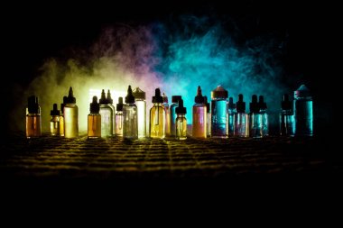 Vape konsepti. Karanlık arka planda duman bulutları ve tüp sıvısı şişeleri. Işık efektleri. Arka plan, vape reklamı ya da vape arkaplan olarak kullanışlı. Seçici odak